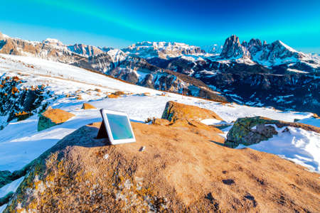 Tablet PC and pen on the Dolomites with rock, snow-capped peaks and conifersの写真素材