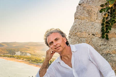 charming middle-aged tanned man in white shirt in a seaside ancient Italian townの写真素材