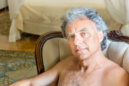 Handsome shirtless tanned man sitting on easy chair in the living roomの写真素材