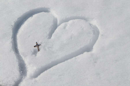 Silver Crucifix left on a heart drawn by hand in the fresh snowの写真素材