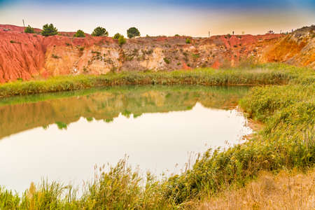 red soils around the freshwater lake formed in a former quarry for the extraction of bauxite in Italyの写真素材