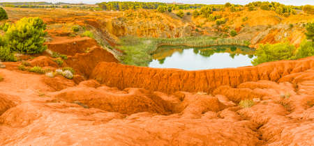 red soils around the freshwater lake formed in a former quarry for the extraction of bauxite in Italyの写真素材