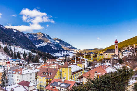 Snowy alpine village in Italy illuminated by sun with mountains in the backgroundの写真素材