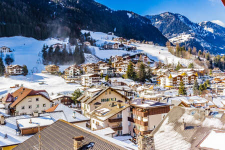 Snowy alpine village in Italy illuminated by sun with mountains in the backgroundの写真素材
