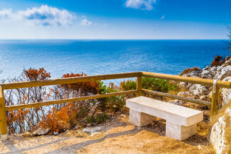 stone bench and wooden parapet on steep cliffs above the sea along the coast of Puglia in Italyの写真素材