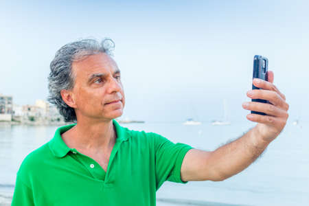 Handsome man in green polo takes a selfie in a seaside town