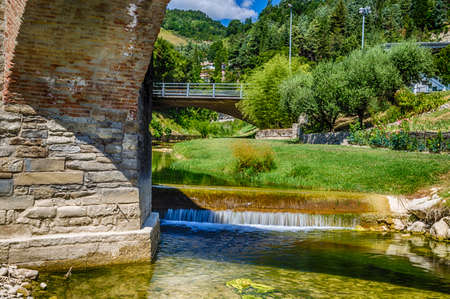 The XVIII century bridge in Modigliana in Italy is overlooking the quiet waters of a small creek with the medieval humpback structure of the three archsの写真素材