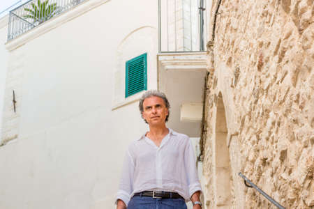 middle-aged man in white shirt while visiting the old streets of ancient town, Vieste in Italy, known as the Pearl of Garganoの写真素材