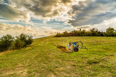 old rusty and dirt plow left on a green but fallow hillの写真素材