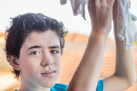 Teenage Boy hangs cotton gloves to dry on a terrace overlooking the rooftops of a village in the countryside in Italyの写真素材
