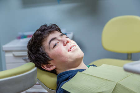 Caucasian teenager with acne skin lying on the dentist chair is smiling showing bracesの写真素材