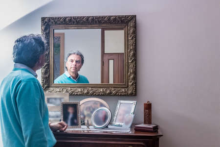 handsome middle-aged man looking in the mirror with nice lookの写真素材