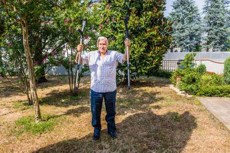 Funny faces of elderly octogenarian male triumphantly holding crutches on the patio of the house