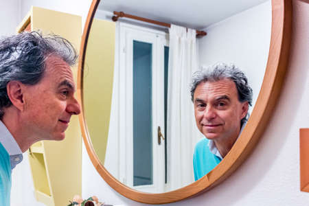 handsome middle-aged man looking in the mirror with nice lookの写真素材