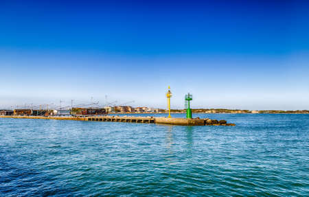 yellow and green lighthouses on the pier crowded with fishing huts facing the palaces of the beach of Romagnaの写真素材