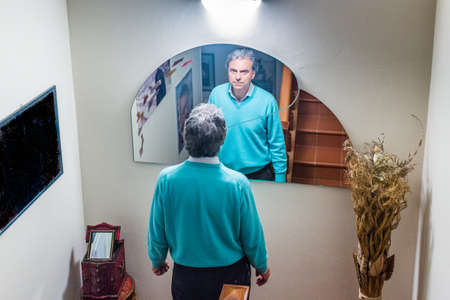 middle-aged man at home looks in the mirrorの写真素材
