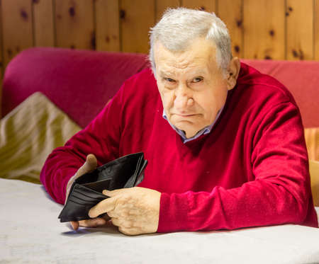 desolate and grim old octogenarian sitting at the kitchen table shows an empty wallet