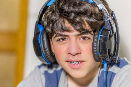 boy with braces wearing headphones while playing with video gamesの写真素材
