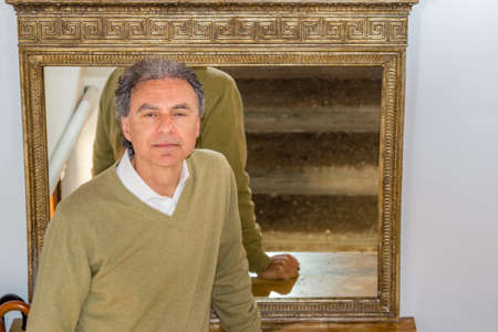 middle-aged man with sleepy, drooping eyelids leaning against  large vintage mirror
