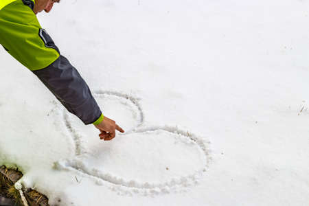 hand of a man who is drawing a heart in the snowの写真素材