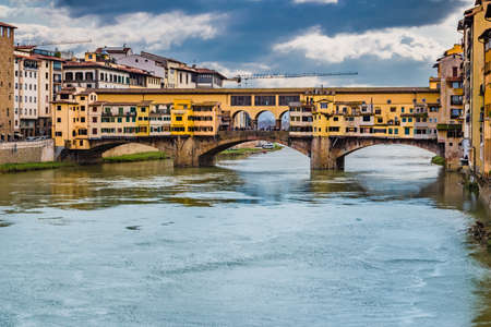 historic buildings overlooking the Arno river that flows peacefully under the arches of the old bridge of Florence on a bright winter dayの写真素材