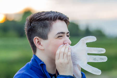 close up of young boy in countryside smiling while blowing in a disposable  plastic glove to inflate itの写真素材