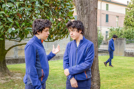 Boys who talk to each other in a garden while another is walking alone, actually the same guy in a multiplicity photoの写真素材