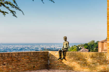 the statue of the boy sitting on the walls of the castle in Longiano Emilia Romagna in front of the panorama of the cultivated landscape of rolling countryside and sea in the distanceのeditorial素材