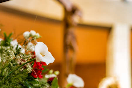 white calla lily in a bouquet of white and red flowers while in the background we see a wood Crucifix of Jesus Christの写真素材