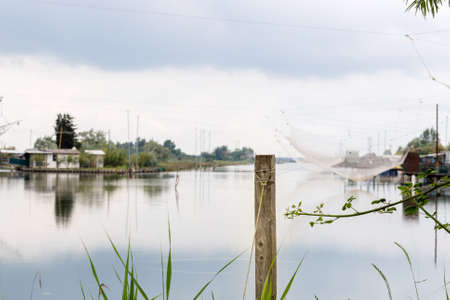wood pole and and fishing huts in the quiet of brackish lagoon in Italyの写真素材