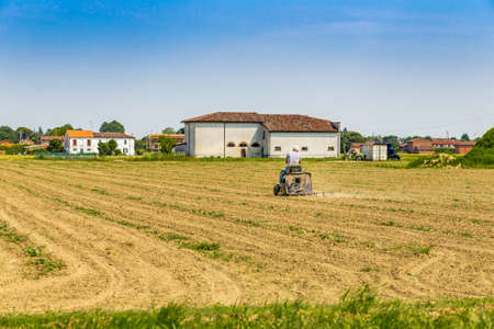 man driving a small tractor plowing a large field in the countryside of Romagna in Italyの写真素材