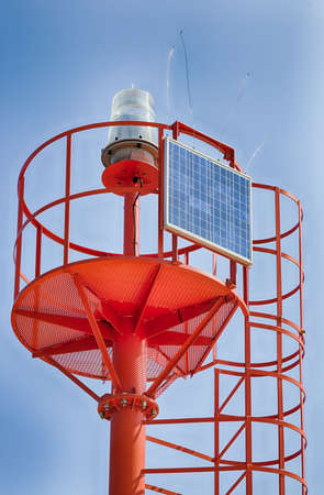 red metal lighthouse powered by solar panelの写真素材