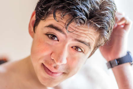 close up of face of just woke up young teen boy in interiors under harsh sun light holding his head