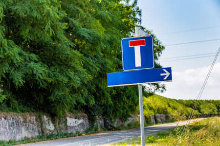 dead end road and direction sign to the right, both without written words, situated on a country road near the bank of a riverの写真素材