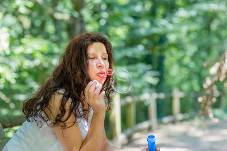 beautiful mature adult woman playing in the park blowing soap bubbles