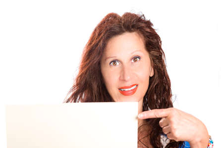 Happy mature woman with wavy brown hair smiles pointing her finger at blank signboard she is holdingの写真素材