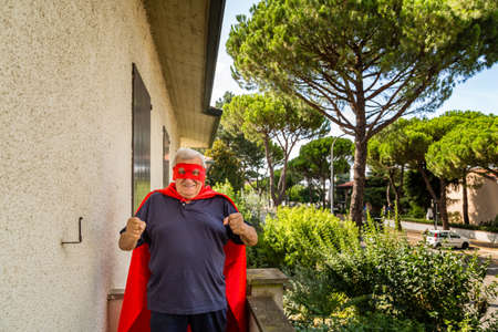 an old man dressed as a superhero on balcony of his house showing fistsの写真素材