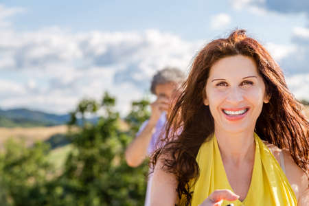 Wife and husband, a mature couple, taking a selfie but while the woman is smiling, the man is rubbing his eyes in the country backgroundの写真素材