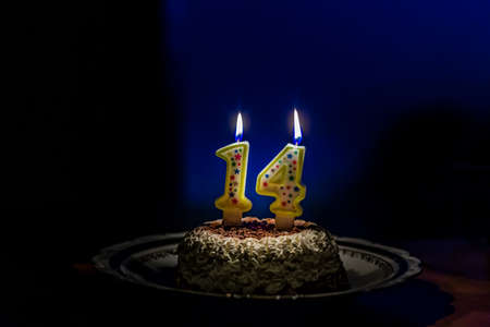 cream and chocolate cake with lit number one and number four candles to celebrate fourteen years...