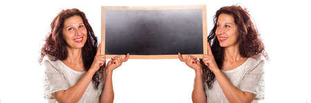 beautiful middle-aged woman with wrinkles and aging skin holding a black chalkboard with a clone of herself in a multiplicity photo isolated on whiteの写真素材