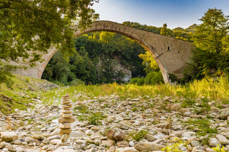 pile of stones in front of 500 years old hog backed Renaissance bridge connecting two banks with single span in Italian Countrysideの写真素材
