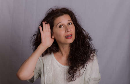 Mature woman placing hand on hear because of hearing problems or impairment on grey backgroundの写真素材