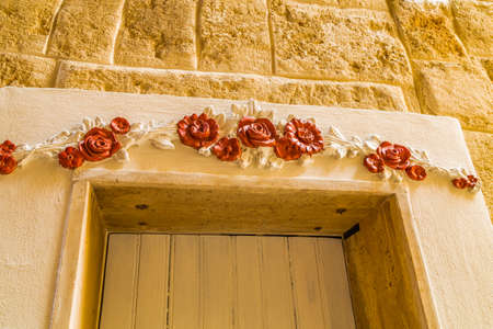 decorated  red flowers and roses on a pediment of a doorの写真素材