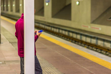 man reading smartphone while leaning on square columnの写真素材