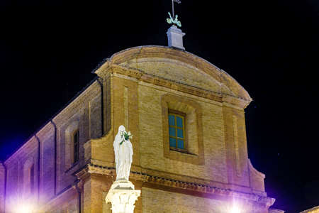 The statue of the Blessed Virgin Mary holding white roses at nightの写真素材