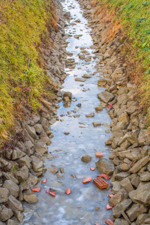 broken red bricks on frozen water of irrigation channel in the countryside of Emilia Romagna in...