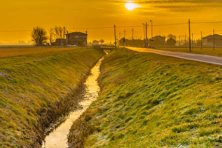 the dawn of the sun rising over an irrigation channel in the countryside of Emilia Romagna in Italyの写真素材