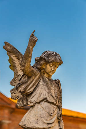 statue of young angel looking down and raising finger up to the skyの写真素材