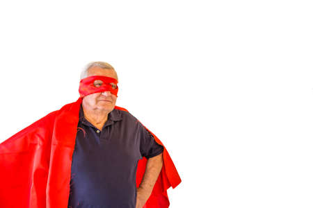 happy elderly man playing superhero with red cape and mask holding fists on hips, isolated on white background,の写真素材