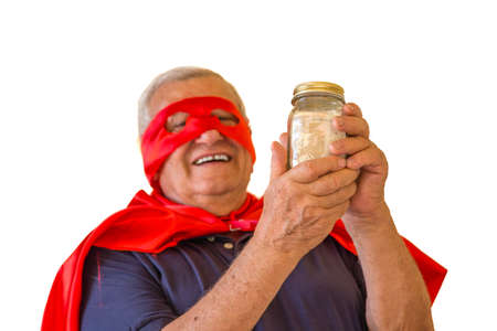 Happy mature man in superhero costume holding a money glass jar filled with euros isolated on white background, concept is that elderly is still powerful with retirement planの写真素材